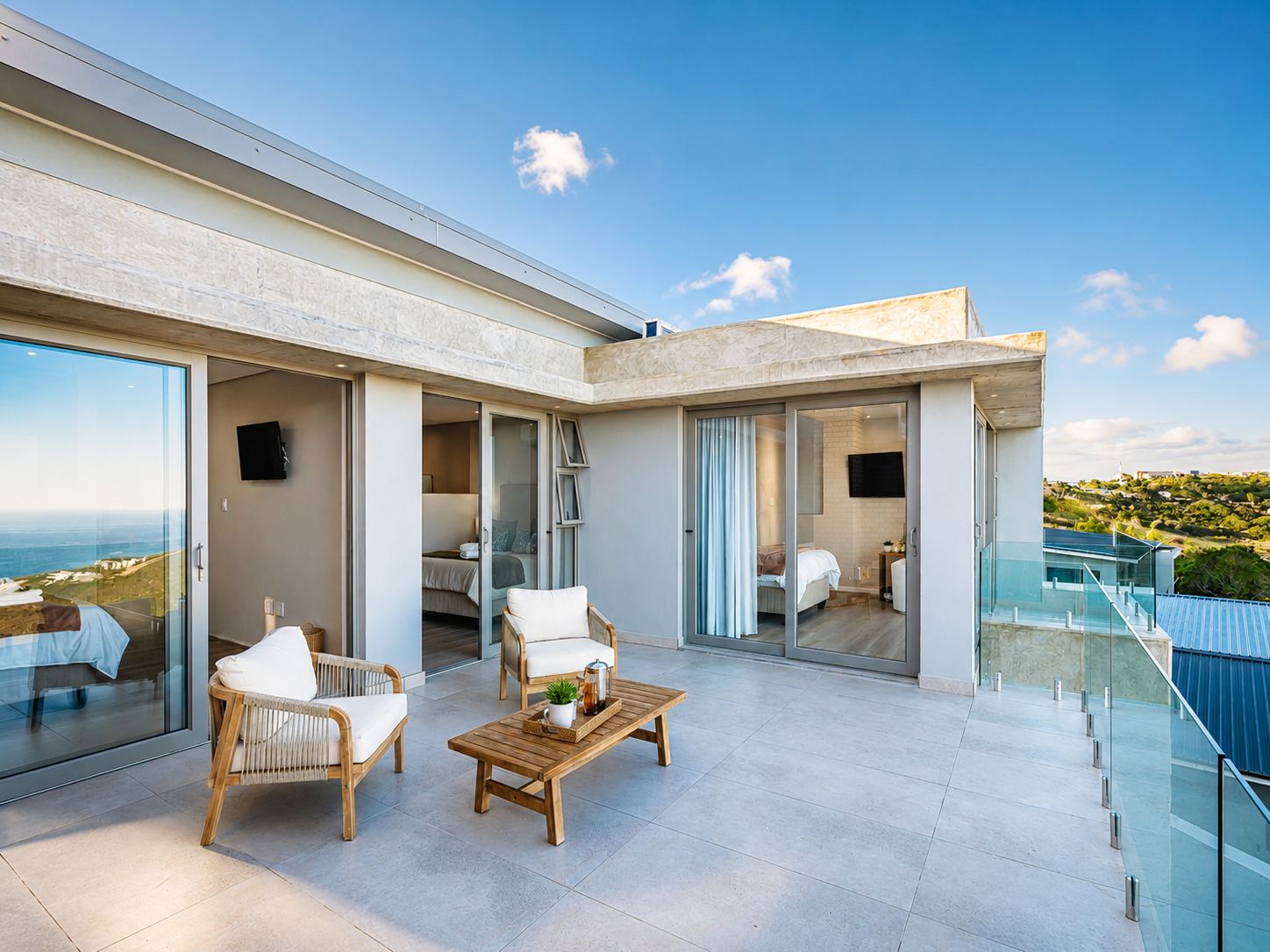 Sunlit villa terrace with lounge chairs and glass railings overlooking the ocean at Dolfyn Villas, Herolds Bay
